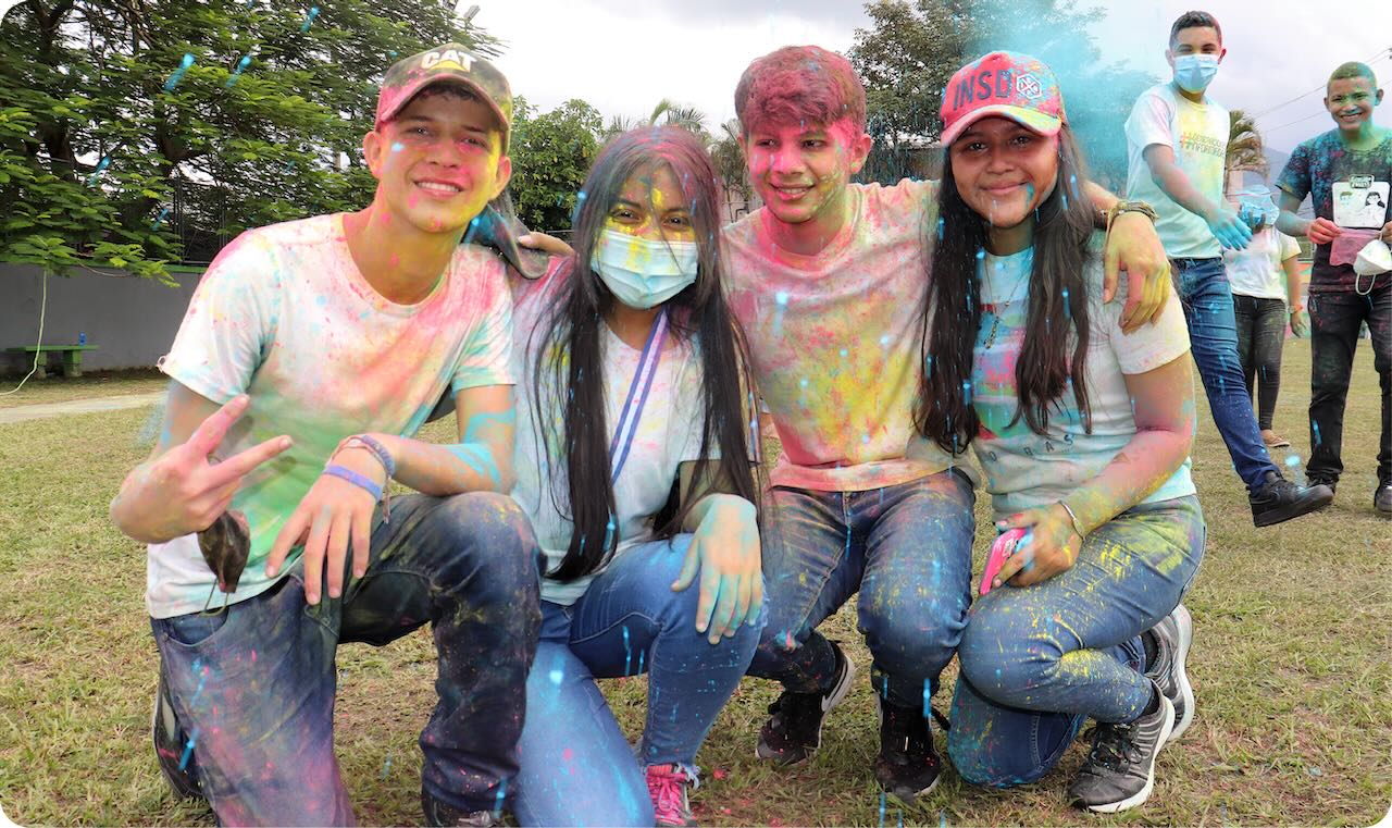 Fotografía: cuatro personas jóvenes posan para una foto cubiertas de pintura, después de una actividad grupal.